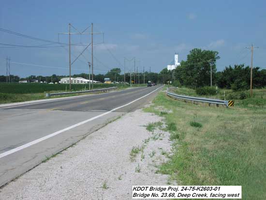 View of bridge from highway; grain elevator in distance; little change in elevation along road