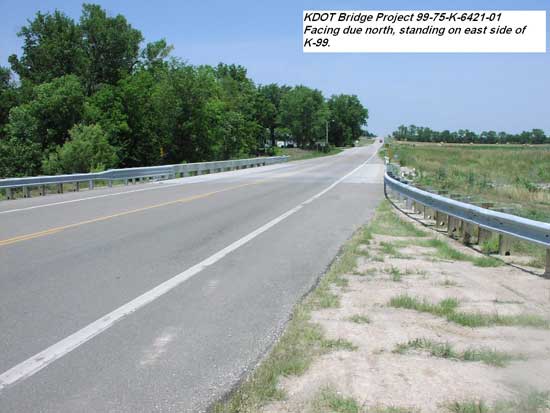 view along highway towards bridge; trees on left and prairie to right