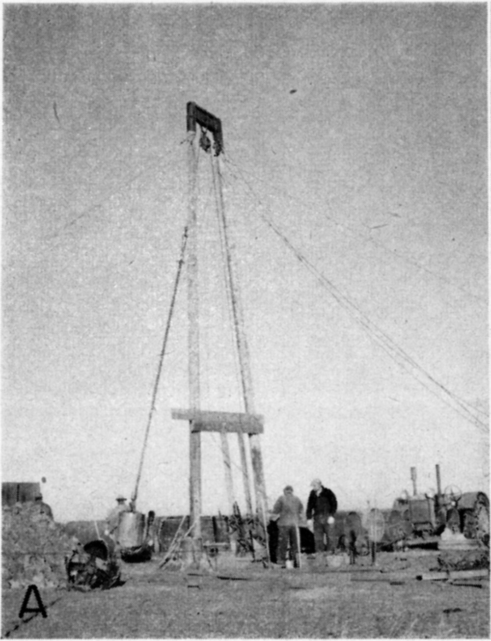 black and white photo of two-legged drilling equipment, held up by cables