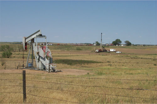 gray pumpjack at producing well; well being plugged in background
