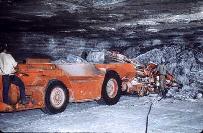 underground salt mine, space is around 12 feet high, with two men operating a drill, cutting away at the face of the salt