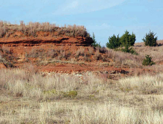 Color photo of steeply sided hill above tall grases, Harper Sandstone.