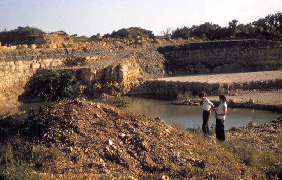 Color photo of limestone quarry; two people overlooking quarry, water in bottom of pit.
