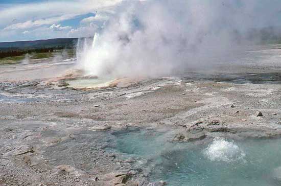Color photo of geyser found in Yellowstone National Park shows hot water bubbling and erupting above the land surface.