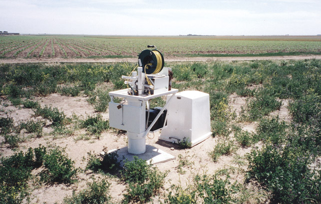 Site in prairie next to cropland; white metal housing contains measuring equipment.