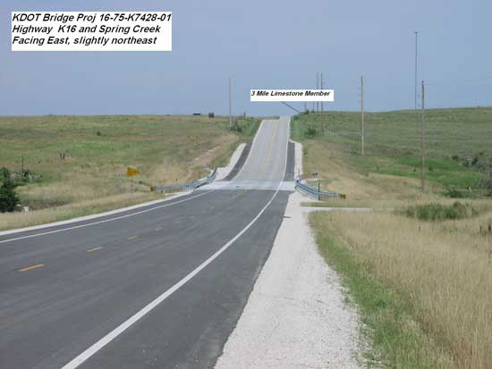 road dips towards bridge and rises after bridge; grassland on either side of road