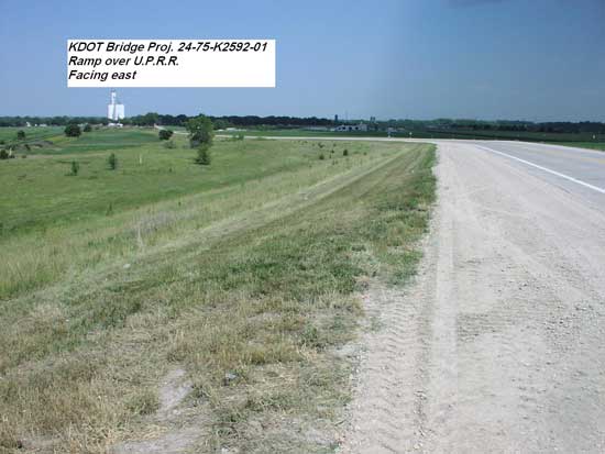 view of road and embankment; road gently curves to left towards town and grain elevator