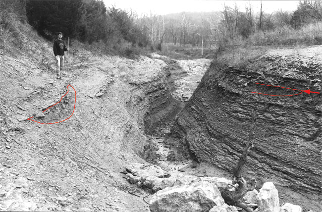 Black and white photograph of student standing above deeply cut channel.