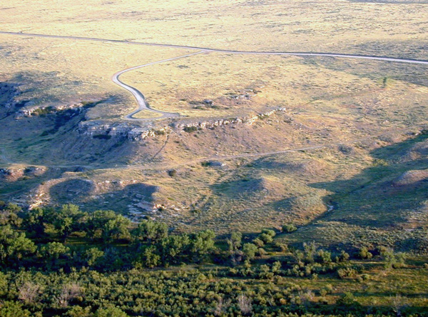 Color aerial photo of rocky bluff in grassland above valley filled with trees.