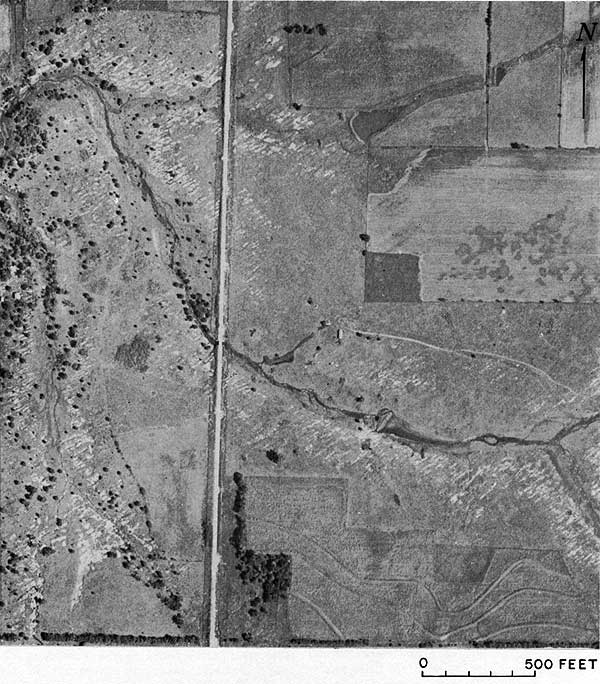 Black and white aerial photo of part of sec. 22, showing grasslands, tilled fields, dirt road, and limestone outcrops mostly striking to NE.