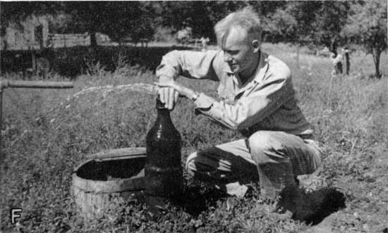 Black and white photo of man showing amount of water flowing from artesian well.