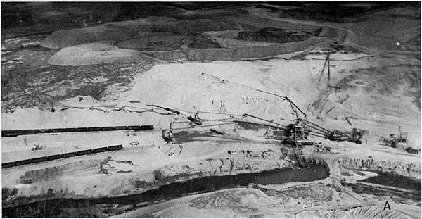 Black and white aerial photo of quarry operations; large conveyor belts move material from sorting-crushing area to waiting train cars.