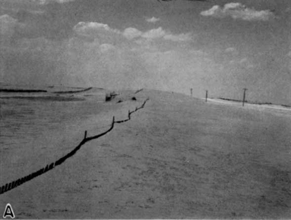 Black and white photo of sand dunes moving over snow fences.