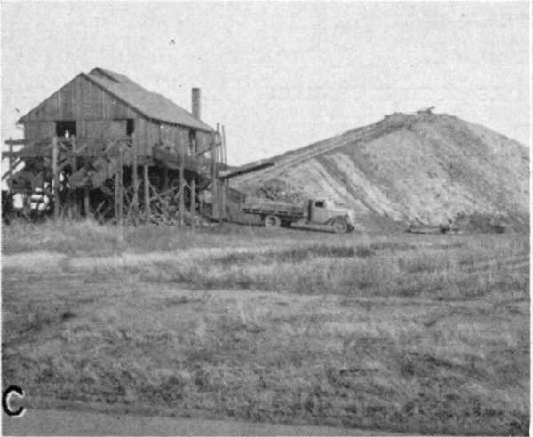 Black and white photo of coal mine; wooden building with truck in foreground; tailings pile in background.