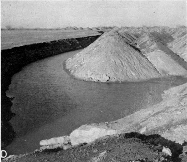Black and white photo of water-filled pit; large tailings piles in center.