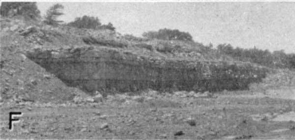 Black and white photo of quarry; hill in background above quarry face 20-30 feet tall.