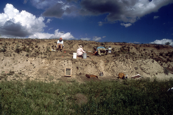 Three people working on side of small hill.