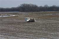 Vibraseis truck in field, snow in crop ridges, new crops browner and dormant