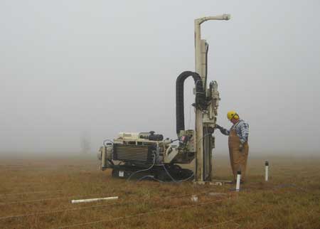 Field geologist using direct-push logging tool; foggy day in field.