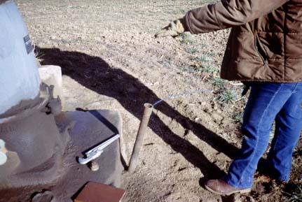 Slant pipe emerges about a foot above the cement pad around well; measuring tape in pipe.