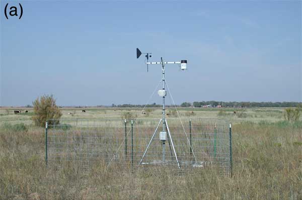 Weather station located in grassland; within small fence; in far background is a house where a secondary weather station was located.