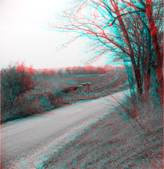 Gravel road curving to right; railroad curving to left through farmland