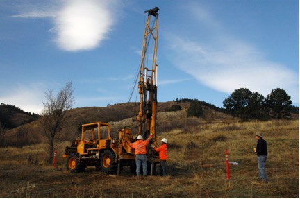 Dr. Mandel stands next to a drill rig at Magic Mountain in 2017