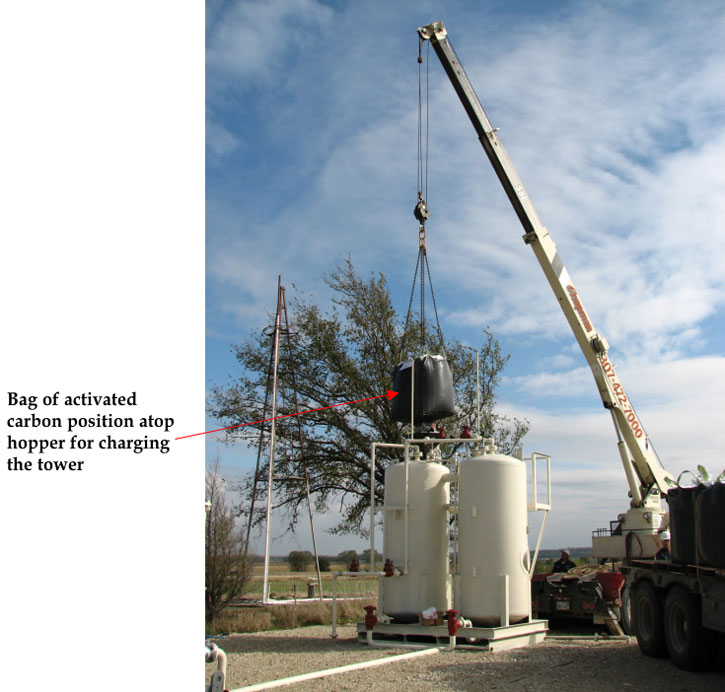 Single boom crane hoisting bag of activted carbon above tank; black funnel is positioned above hole in top of tank.