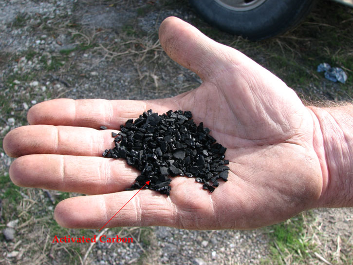 Closeup in palm of hand of the activated carbon granules; shiny black, pieces are rectangular and platy, not rounded at all; pea size or smaller.