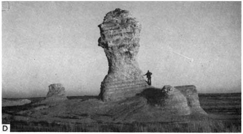Black and white photo man next to formation, about 6-times as tall as the person, next to two two smaller humps of chalk.
