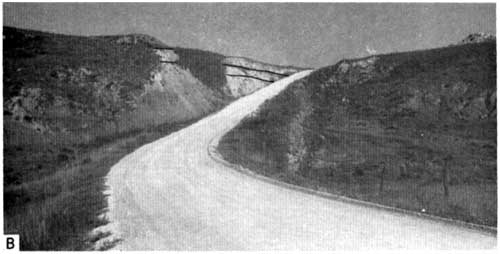 Black and white photo of dirt road curving up a hill; on left side is roadcut with beds outlined.