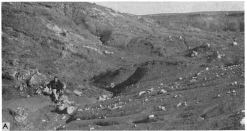 Black and white photo of dry arroyo; man stinning near small (basketball-sized) boulders).