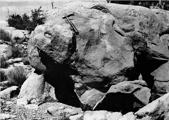 Black and white photo of sandstone boulder, rock hammer for scale.