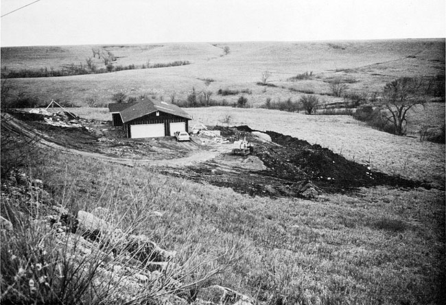 Photo of small home in hilly country; ground is being leveled below house.