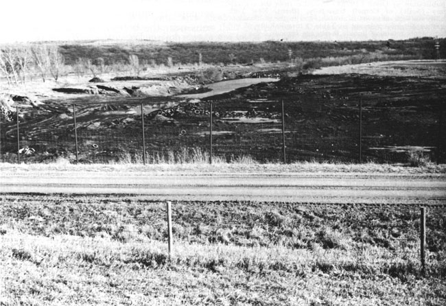 Photo of large fenced landfill, small line of hills in background.