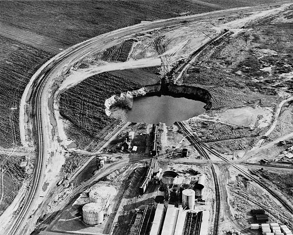 Photograph from air of sinkhole; train tracks have been removed from sinkhole, new track goes around sinkhole.