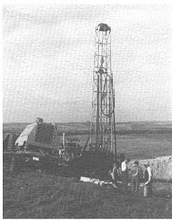 drill rig on hill overlooking river valley; three men in foreground