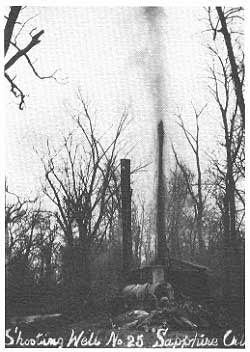 black and white photo small drilling rig, small spray of oil from top of rig, in treeless forest, labeled Sapphire Oil well no. 25
