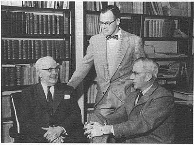 three men speaking together in an office, bookshelves in background, Moore and Foley sitting, Hambleton standing behind