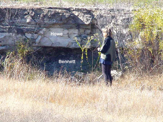 Color photo of researcher standing next to outcrop with Howe and Bennett members shown.