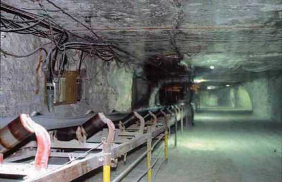 Color photo of salt mine, long room with pillars at sides; conveyor belt to left.