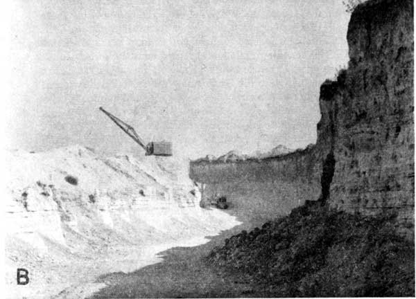 Black and white photo of shovel working in quarry with vertical cliffs to right.