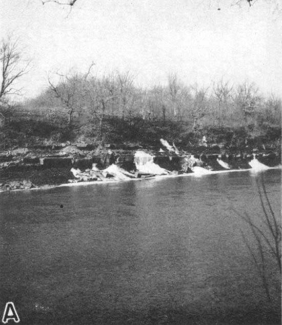 View of sandstone outcrop located across river; looks like winter view based on leaveless trees above bank; water flowimng from sandstone bed is frozen.