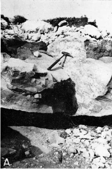 Black and white photo of quartzite boulder, 2-3 feet high, rock hammer for scale.