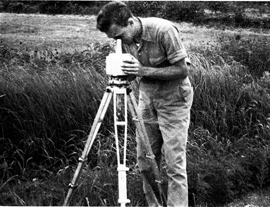 Black and whtie photoo of worker looking down through eyepiece to read magnetic values.