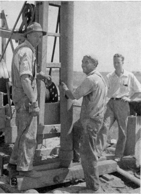Black kand white photo; two men setting casing (8 inches in diameter?) in well; third man in short sleaves observing.