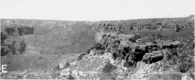 Black and white photo of rugged landscape with buttes along a depression.
