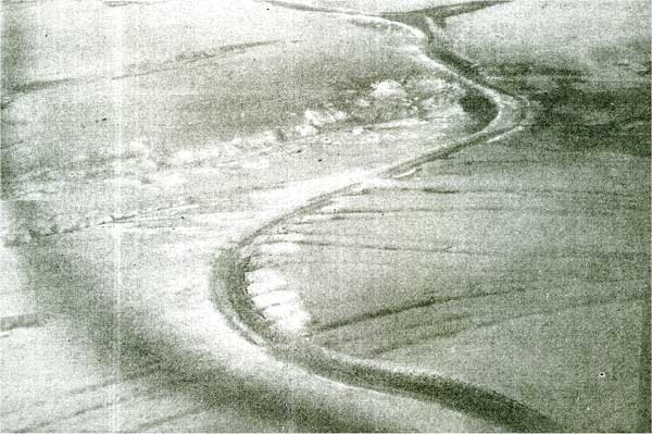 Black and white image of ruts going down a hill and crossing a canal.