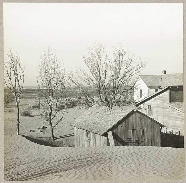 Black and white photo of farmstead overcome by sand dunes.
