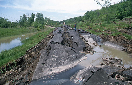 Color photo of a two-lane backtop road destroyed by a landslide.